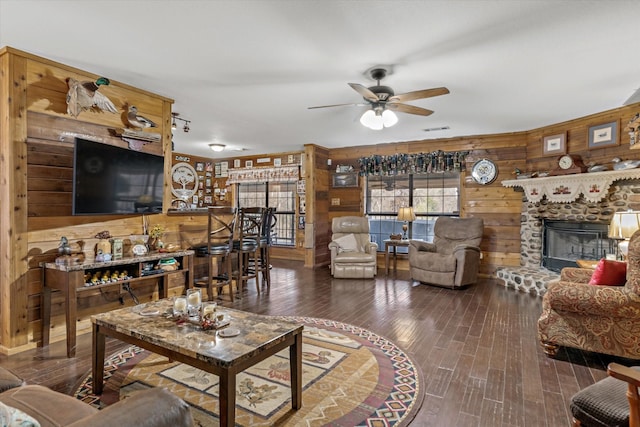 living area with a fireplace, visible vents, a ceiling fan, wood walls, and wood finished floors