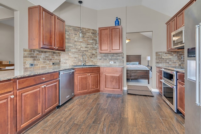 kitchen with lofted ceiling, light stone counters, dark wood-style flooring, a sink, and appliances with stainless steel finishes