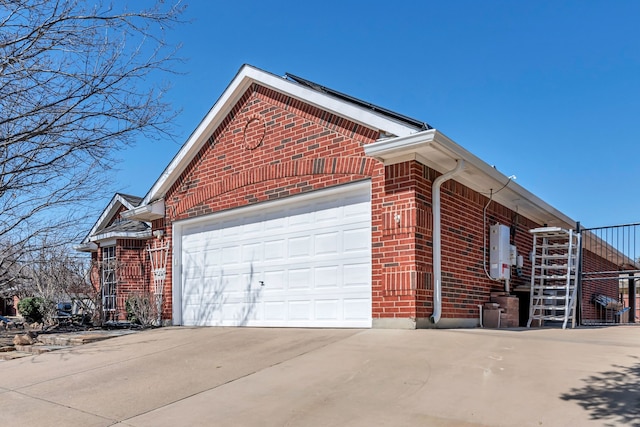 view of side of home featuring concrete driveway, brick siding, an attached garage, and water heater