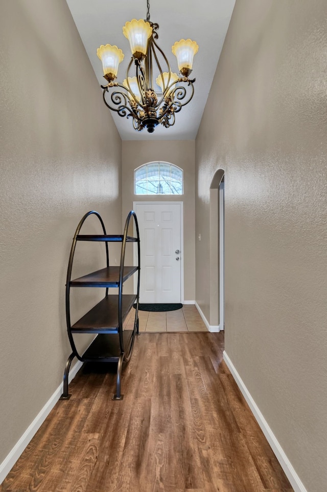 foyer featuring baseboards, a chandelier, arched walkways, and wood finished floors