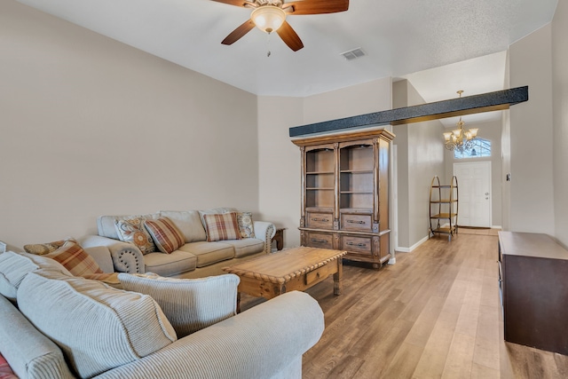 living area with ceiling fan with notable chandelier, baseboards, visible vents, and light wood-style floors