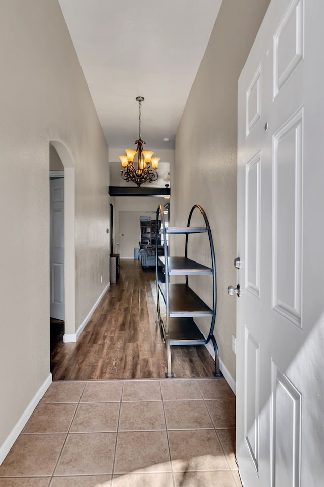 hallway with an inviting chandelier, baseboards, arched walkways, and tile patterned floors