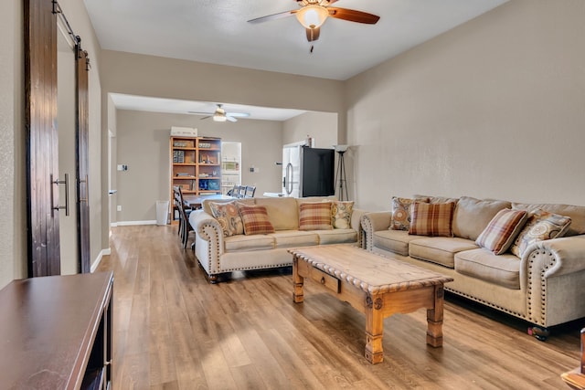 living room featuring light wood-style floors, ceiling fan, baseboards, and a barn door