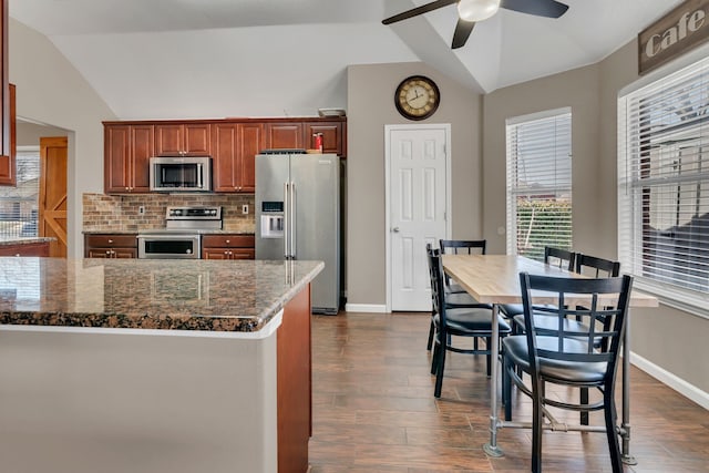 kitchen with dark wood-style flooring, stainless steel appliances, decorative backsplash, vaulted ceiling, and dark stone counters