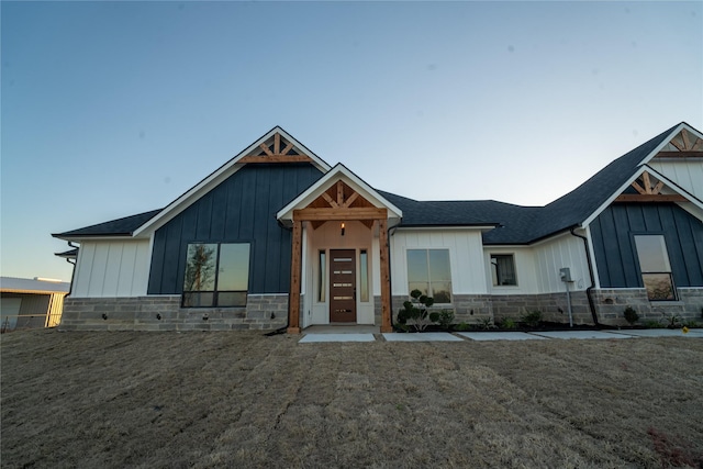 modern inspired farmhouse featuring stone siding, a front lawn, board and batten siding, and roof with shingles