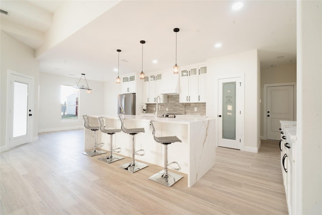 kitchen with tasteful backsplash, stainless steel fridge with ice dispenser, a spacious island, a kitchen breakfast bar, and white cabinetry