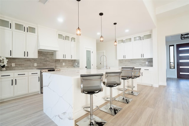 kitchen featuring a kitchen breakfast bar, a kitchen island with sink, stainless steel electric range, custom exhaust hood, and a sink