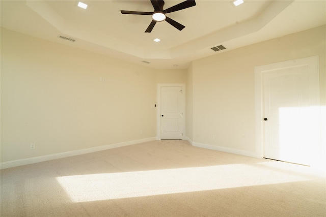 unfurnished room with a raised ceiling, visible vents, light carpet, and baseboards