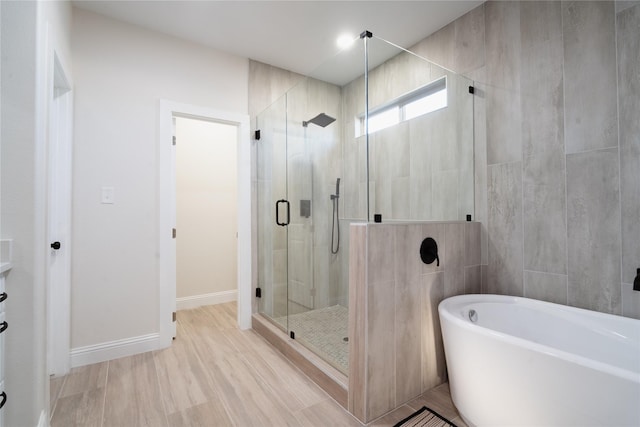 bathroom with tile walls, a shower stall, wood finished floors, a freestanding tub, and baseboards