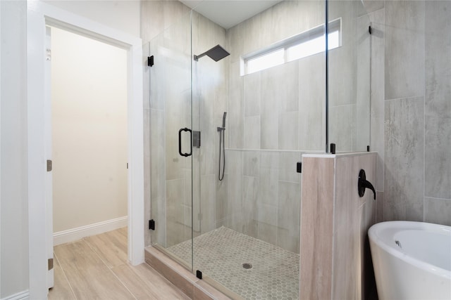 bathroom featuring baseboards, wood finished floors, a freestanding tub, and a shower stall