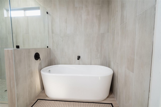 bathroom featuring tile patterned flooring, a freestanding bath, tile walls, and a walk in shower