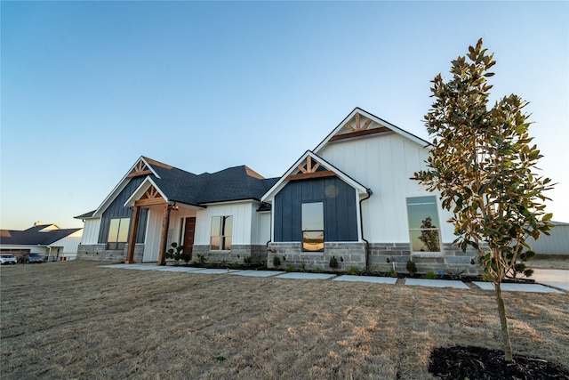 modern inspired farmhouse with board and batten siding, a front yard, stone siding, and a shingled roof