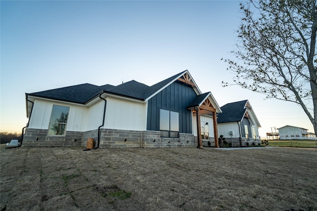 view of front of house with stone siding, a shingled roof, board and batten siding, and a front yard