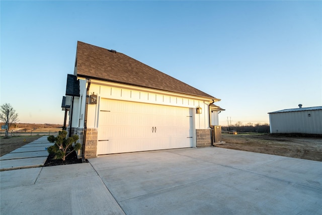 view of side of property with a garage, roof with shingles, board and batten siding, and stone siding