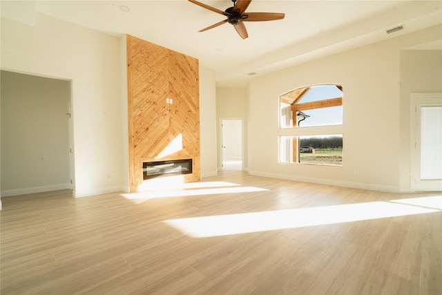 unfurnished living room featuring visible vents, a towering ceiling, light wood-style floors, a ceiling fan, and a large fireplace