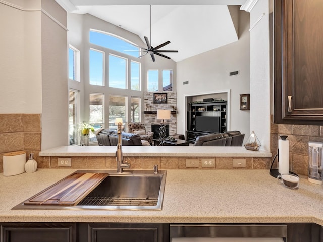 kitchen with a fireplace, a sink, a ceiling fan, open floor plan, and dark brown cabinets