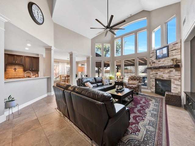 living room featuring light tile patterned floors, baseboards, ceiling fan, ornate columns, and a fireplace