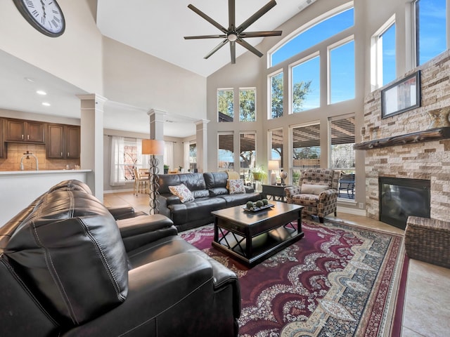 living area featuring decorative columns, light tile patterned flooring, a ceiling fan, and a stone fireplace