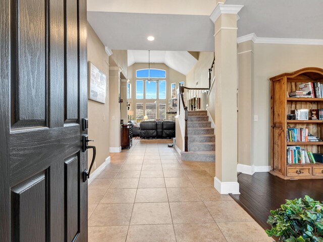 entryway featuring light tile patterned floors, crown molding, baseboards, stairs, and ornate columns