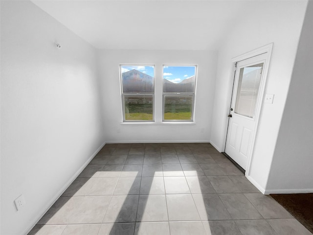 tiled empty room with vaulted ceiling and baseboards