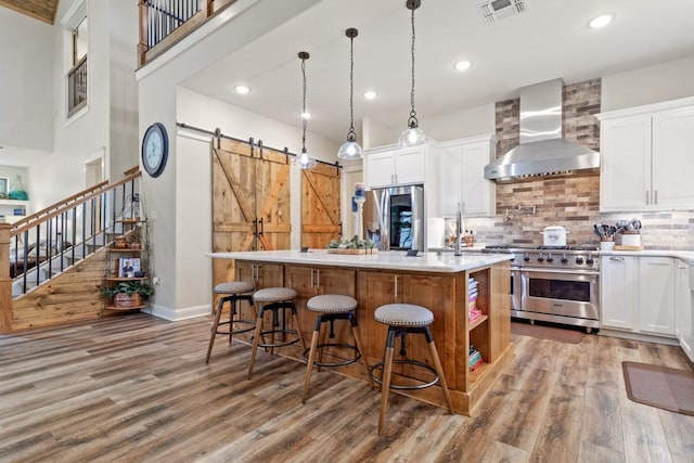 kitchen with wall chimney exhaust hood, appliances with stainless steel finishes, wood finished floors, and visible vents