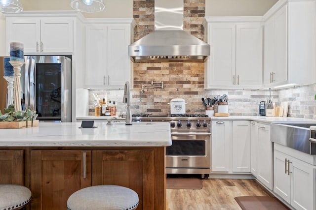 kitchen with stainless steel appliances, wall chimney range hood, decorative backsplash, and white cabinets