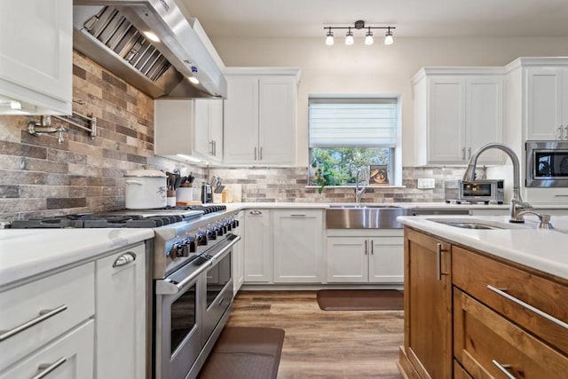 kitchen featuring stainless steel appliances, backsplash, white cabinetry, a sink, and wall chimney exhaust hood