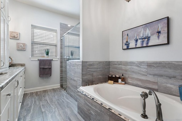 bathroom with a stall shower, baseboards, a bath, and vanity