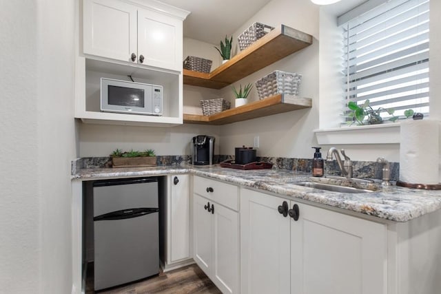 kitchen featuring refrigerator, open shelves, white microwave, white cabinetry, and a sink