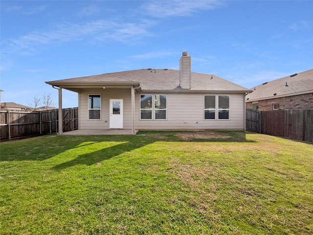 rear view of house with a fenced backyard, a yard, a chimney, and a patio