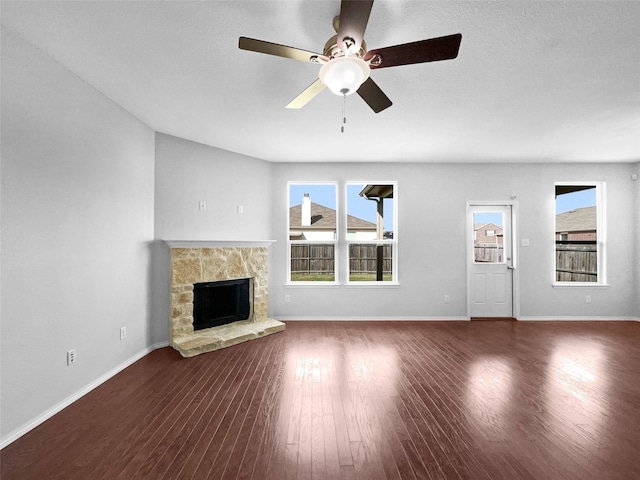 unfurnished living room with ceiling fan, baseboards, wood finished floors, and a stone fireplace