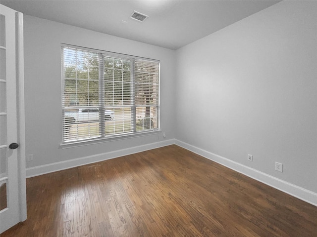 unfurnished room featuring dark wood finished floors, visible vents, and baseboards