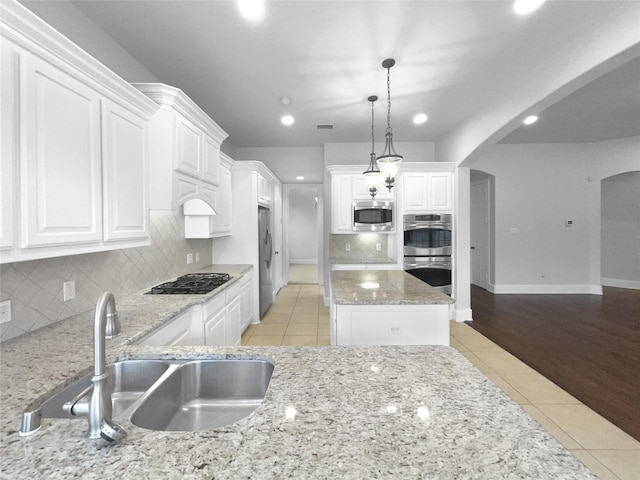 kitchen with light tile patterned floors, arched walkways, appliances with stainless steel finishes, white cabinetry, and a sink