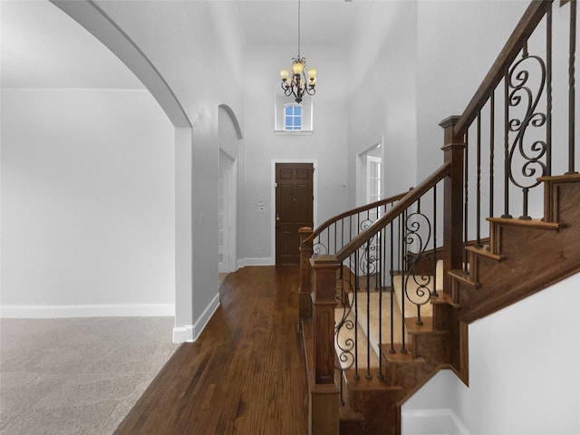 entrance foyer featuring arched walkways, a high ceiling, an inviting chandelier, baseboards, and stairs