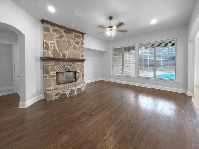 unfurnished living room featuring arched walkways, a fireplace, baseboards, and wood finished floors