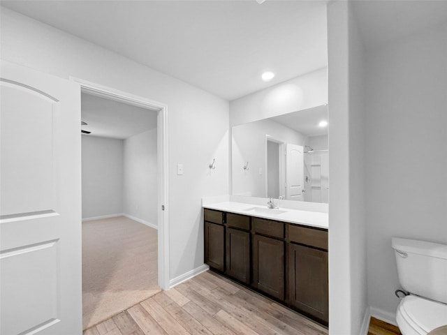 bathroom with toilet, recessed lighting, wood finished floors, vanity, and baseboards