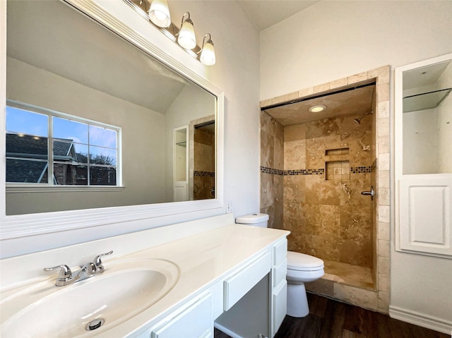 full bath featuring tiled shower, vanity, toilet, and wood finished floors