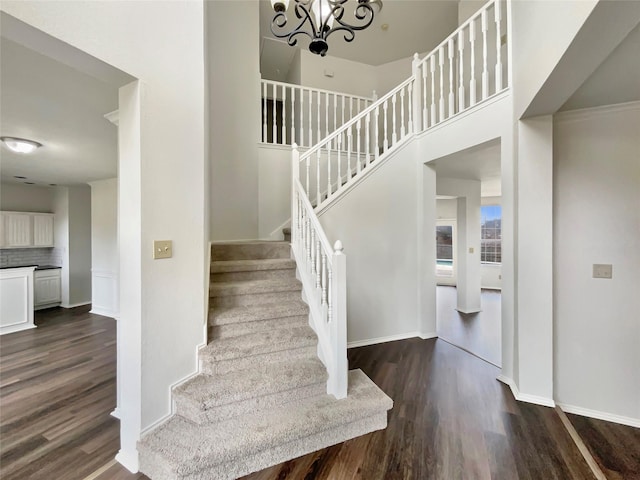 stairs with a chandelier, wood finished floors, a towering ceiling, and baseboards