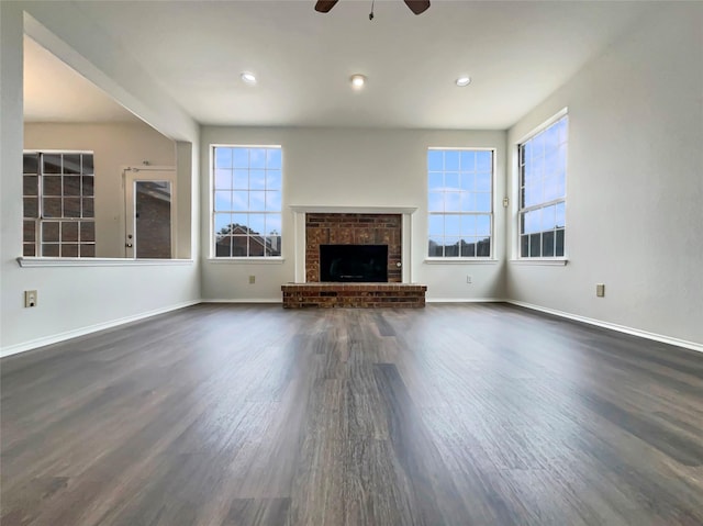 unfurnished living room featuring dark wood-type flooring, plenty of natural light, a fireplace, and baseboards