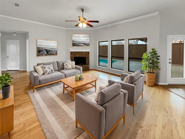 living room featuring a fireplace with raised hearth, light wood finished floors, visible vents, and crown molding