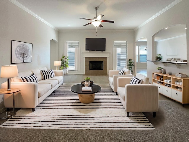 living room featuring ceiling fan, a fireplace, arched walkways, and crown molding