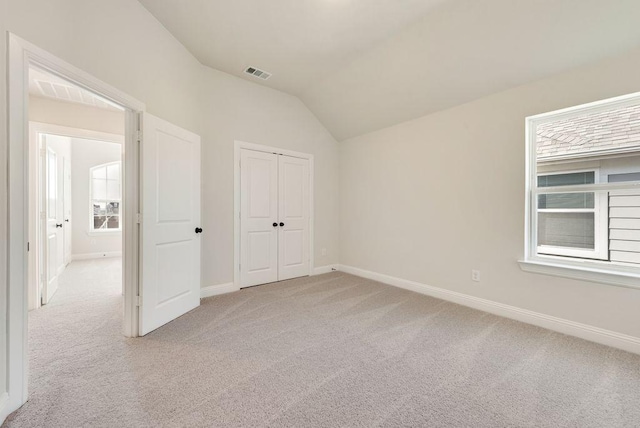 unfurnished bedroom featuring light carpet, multiple windows, visible vents, and vaulted ceiling