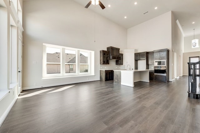 unfurnished living room featuring ceiling fan, dark wood-type flooring, a high ceiling, a sink, and visible vents