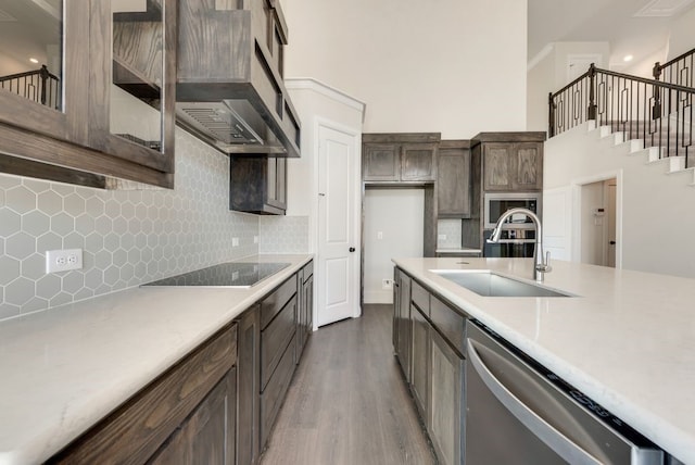 kitchen with a sink, a towering ceiling, light countertops, appliances with stainless steel finishes, and dark wood finished floors