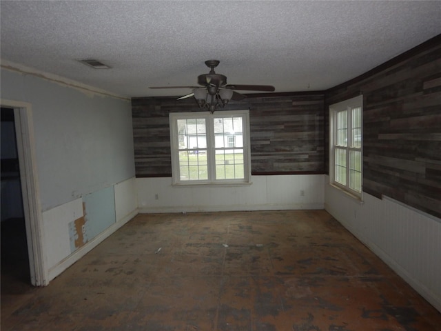 spare room with a textured ceiling, ceiling fan, wainscoting, and visible vents