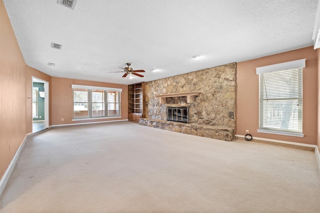 unfurnished living room with carpet floors, baseboards, a stone fireplace, and a textured ceiling