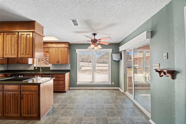 kitchen featuring brown cabinetry, dark countertops, visible vents, and a sink