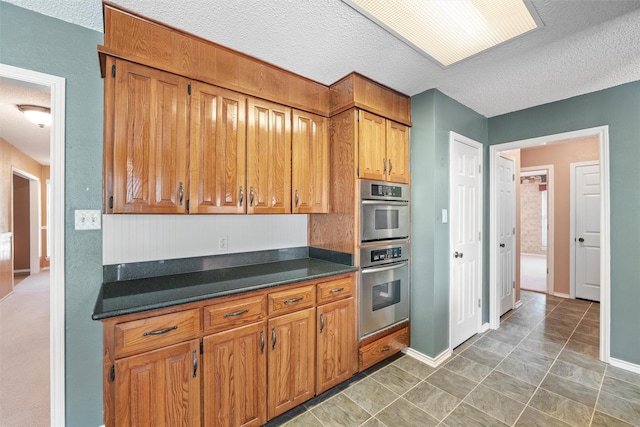 kitchen featuring dark countertops, a textured ceiling, brown cabinets, and stainless steel double oven