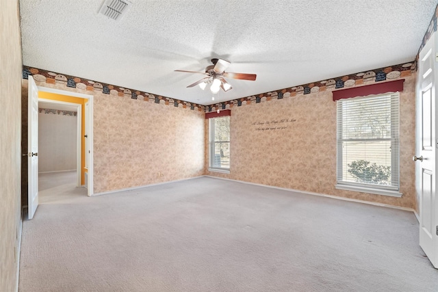 carpeted spare room with a textured ceiling, visible vents, and a ceiling fan