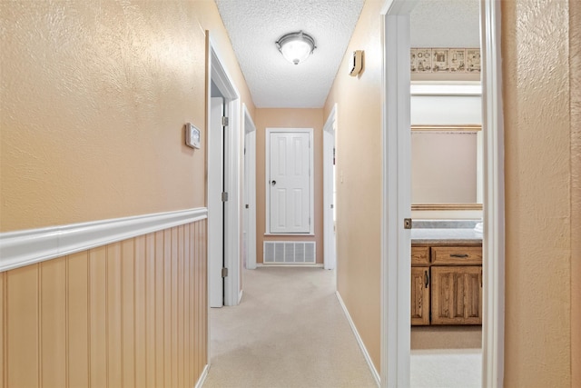 hall featuring light carpet, visible vents, a textured ceiling, and wainscoting